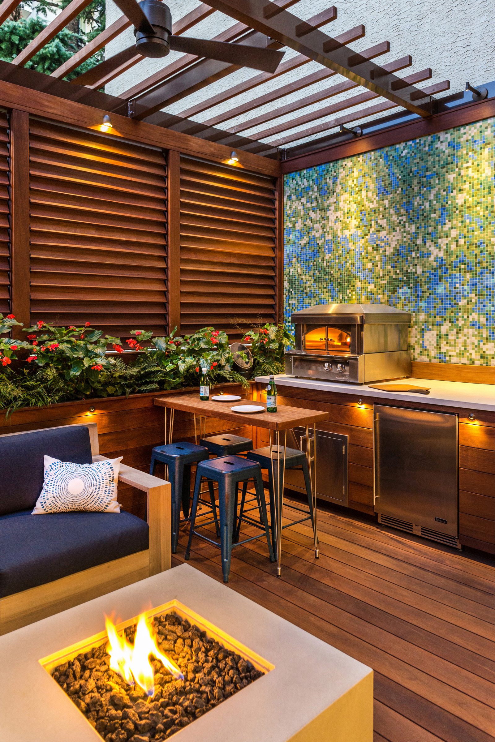 An outdoor lounge with a pergola, fire table and discreet lighting around the seating and kitchen